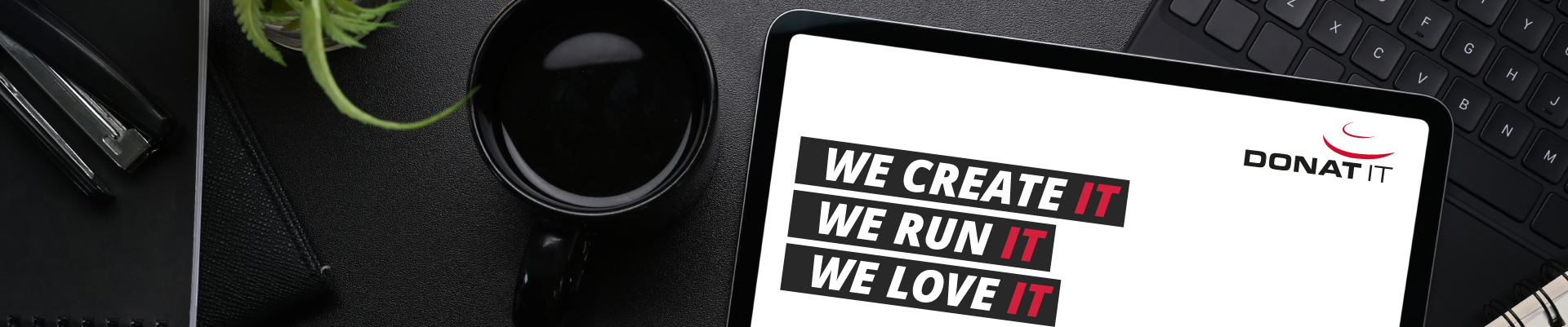 Schreibtisch mit Tablet, das DONAT IT Slogan "We create IT, we run IT, we love IT" anzeigt. 
